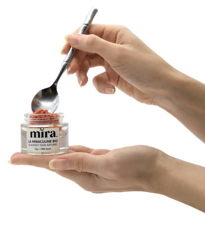 Photo du pot Mira® contenant les 10 g de poudre de Miraculine posé sur une main avec un utilisateur en train de se servir grâce à une cuillère. Produit 100% naturel issu de baie Miracle.